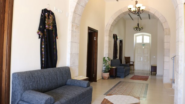 A spacious lobby with a grey sofa, a chandelier, and a large window. - Ma'an lil-Hayat Boutique Hotel  (Bethlehem)
