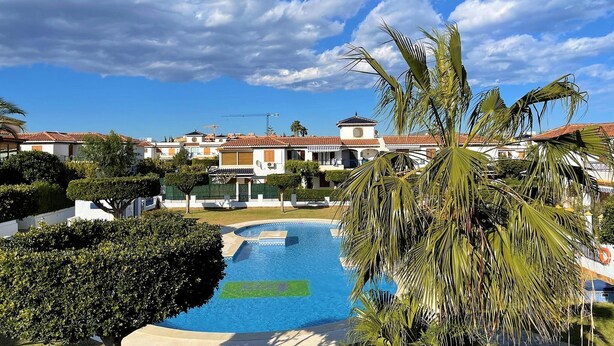 A swimming pool surrounded by well-maintained greenery and buildings with red-tiled roofs. - Apartment in Vera Playa near the Beach (Vera Playa)