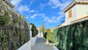 A narrow pathway flanked by white walls and green hedges leading to a building with a tiled roof. - Apartment in Vera Playa near the Beach (Vera Playa)