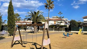 A playground with swings and a climbing structure, surrounded by palm trees and buildings with red-tiled roofs. - Apartment in Vera Playa near the Beach (Vera Playa)