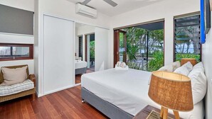 A modern bedroom with a large bed, a ceiling fan, and a view of greenery outside. - Onda Beach Holiday Home in Clifton Beach (Clifton Beach)