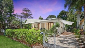 A modern house with a covered patio, surrounded by lush greenery and a well-maintained lawn. - Onda Beach Holiday Home in Clifton Beach (Clifton Beach)