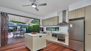 A modern kitchen with a central island, stainless steel appliances, and a dining area with outdoor seating. - Onda Beach Holiday Home in Clifton Beach (Clifton Beach)