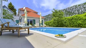 A swimming pool with lounge chairs and a plate of fruit.
