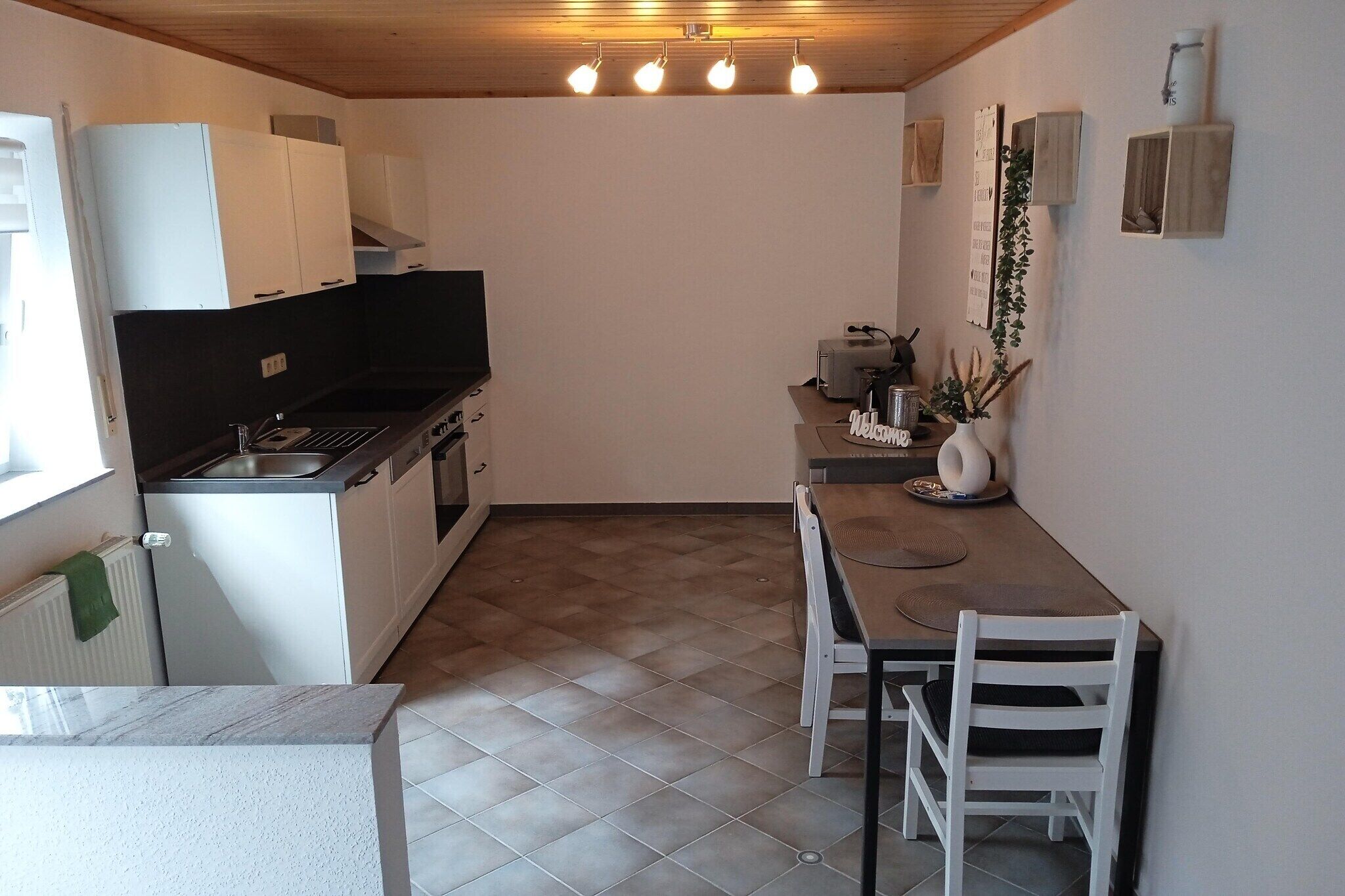 Una cocina compacta con armarios blancos, encimera negra y una zona de comedor con mesa y sillas.