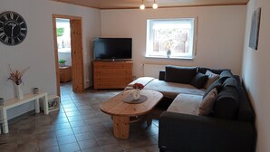 A living room with a wooden ceiling, a TV on a wooden cabinet, a sofa, a coffee table, and a clock on the wall. - Tranquil Getaway in Scenic Roes (Roes)