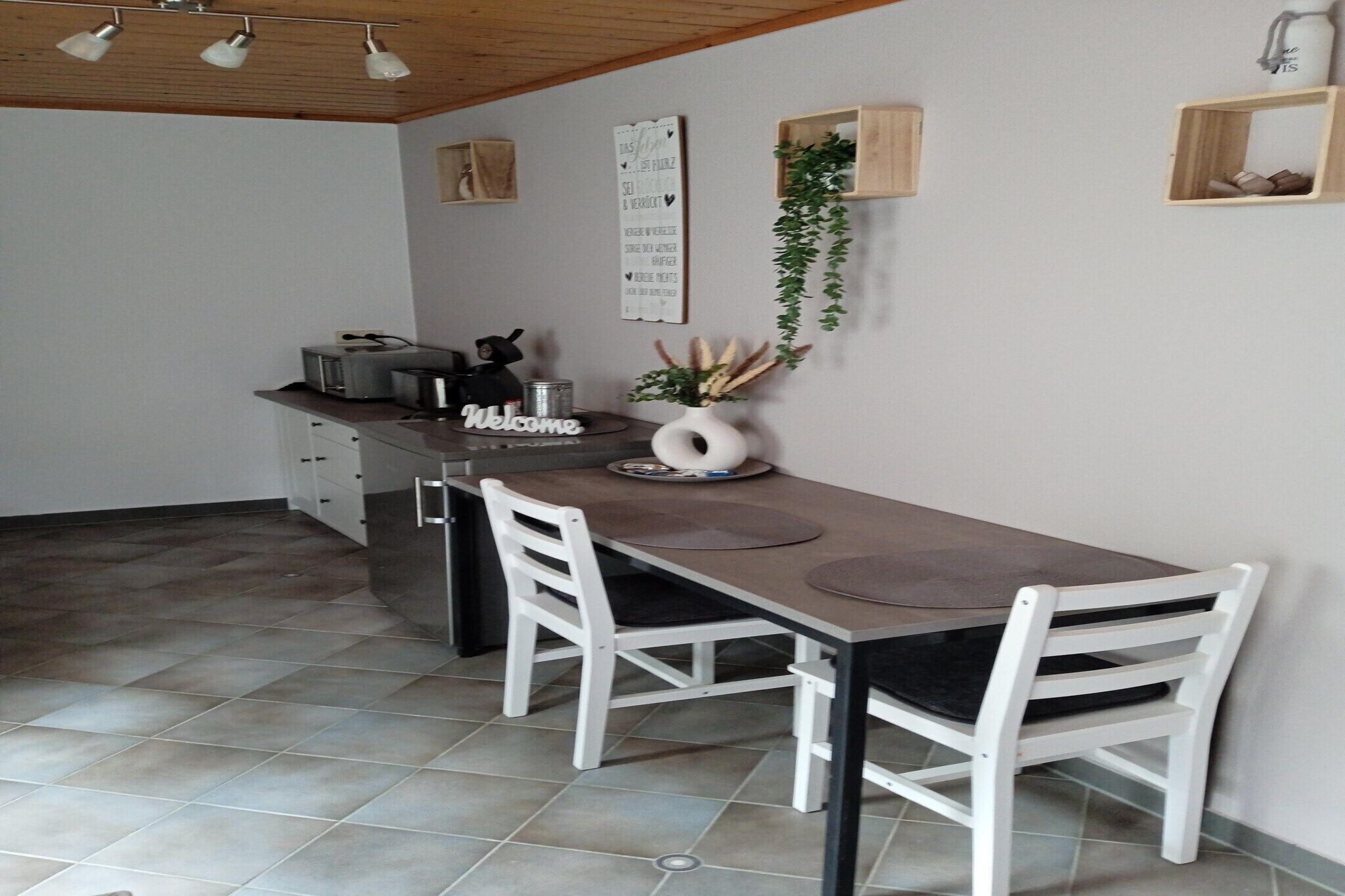 A small, modern kitchen with a dining table, two white chairs, a toaster, and a welcome sign.