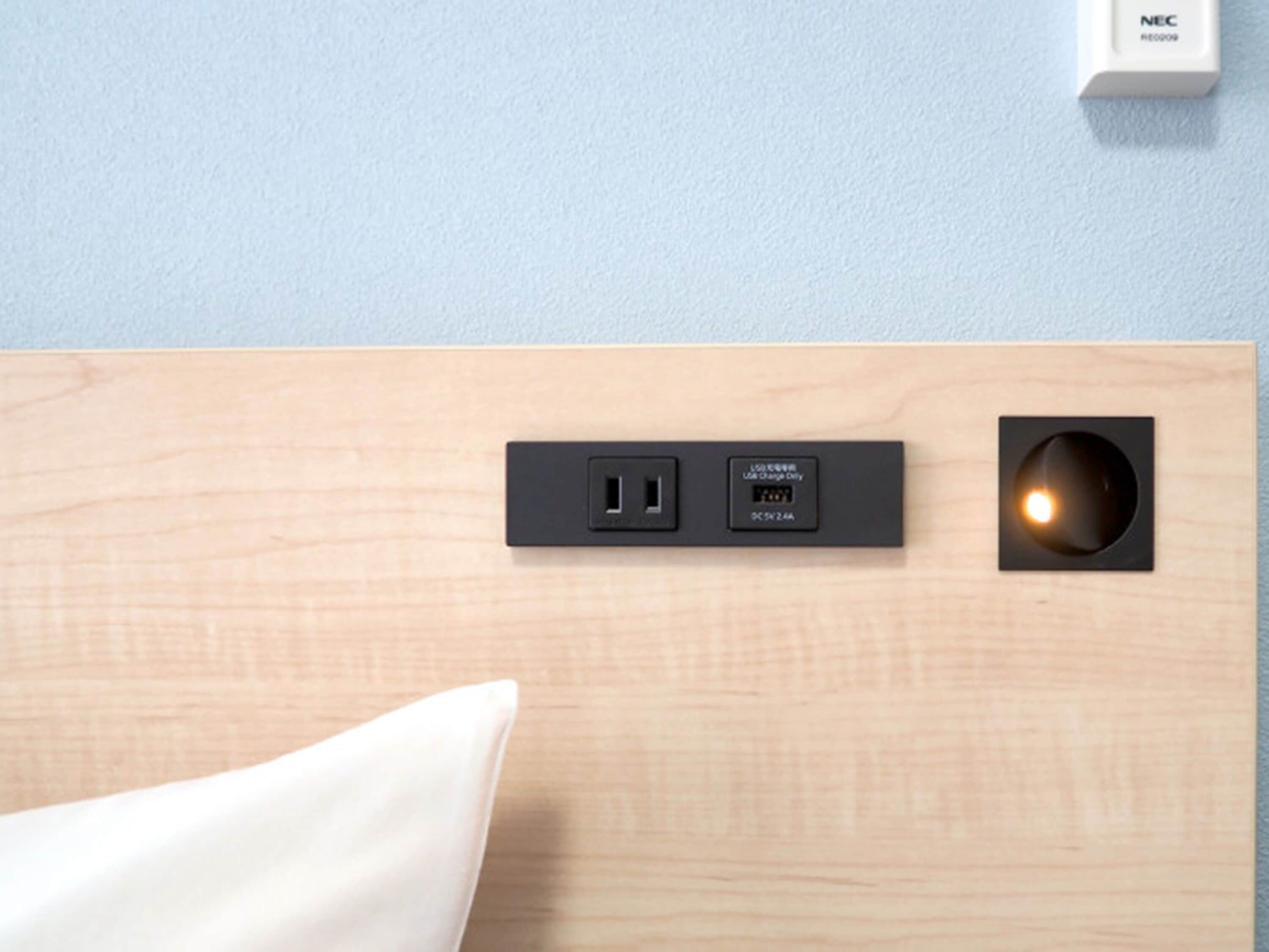 A wall-mounted power strip with a USB port and a wall socket, a recessed light fixture, and a white wall switch labeled "NEC".