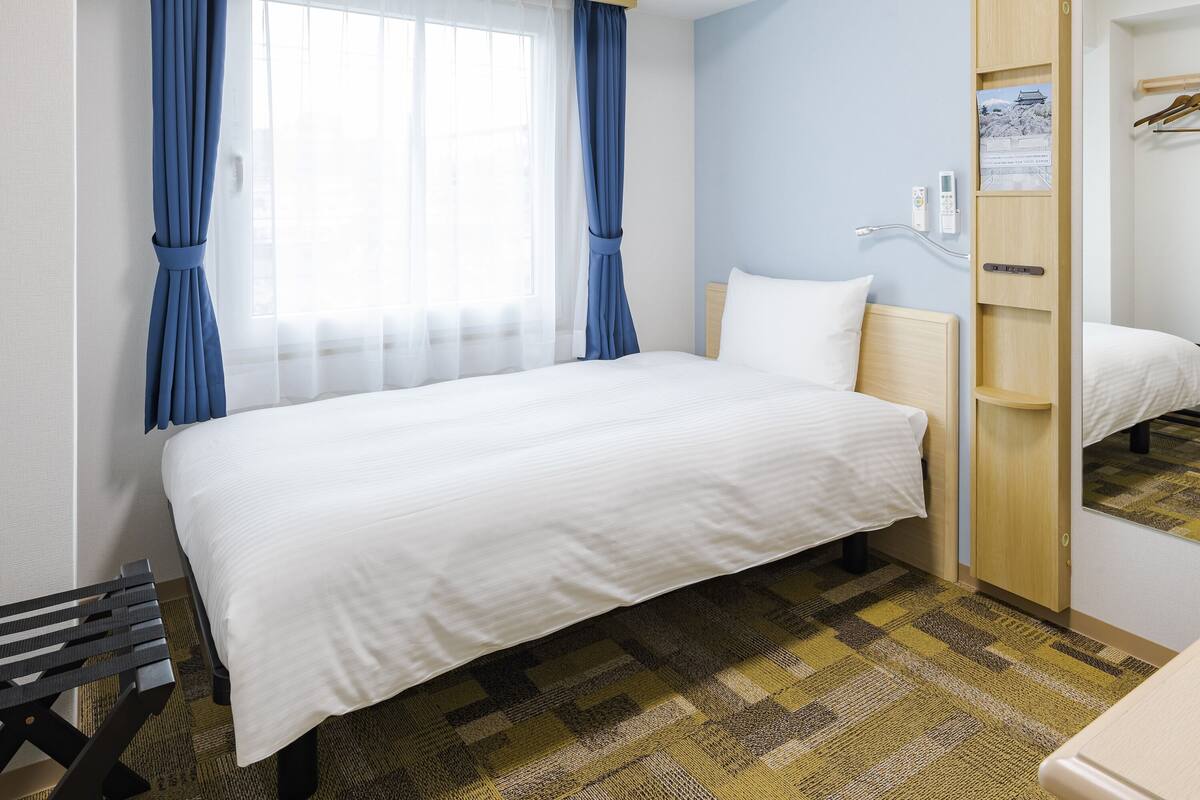 A hotel room with a bed, a desk, and a wardrobe.