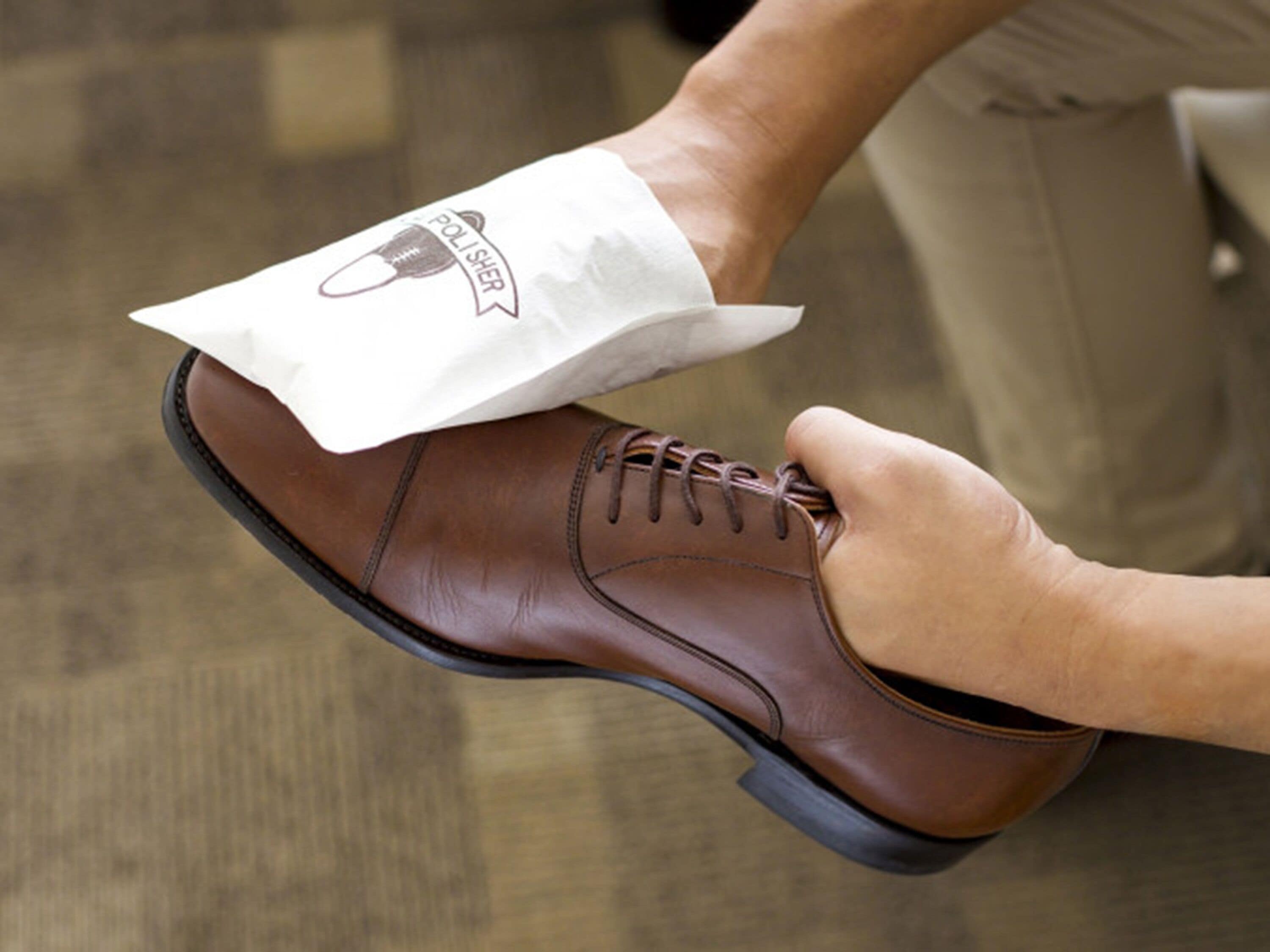Une personne porte une chaussure en cuir marron avec une manche en tissu blanc ornée d’un logo.