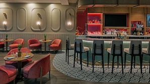 Een bar met een gebogen toonbank, rode en zwarte stoelen en een patroon vloer.