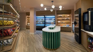Een moderne winkelruimte met schappen vol snacks en drankjes, een centraal bedieningspunt en een koelvitrine op de achtergrond.