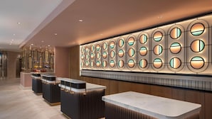 Een moderne hotellobby met een receptiebalie, een wand met ronde lichtarmaturen en een decoratieve spiegelwand.