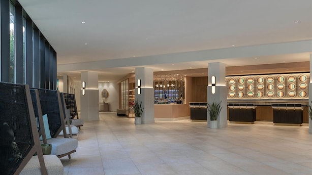 Een ruime lobby met hoge plafonds, moderne zitplaatsen en een receptiehoek met een decoratieve verlichtingsarmatuur.
