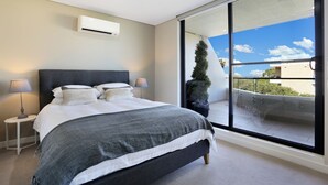A modern bedroom with a large bed, bedside lamps, and a view of the outdoors through a sliding glass door.