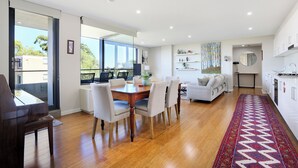 A modern kitchen with white cabinets, a dining area with a wooden table and chairs, and a living area with a sofa and a coffee table.