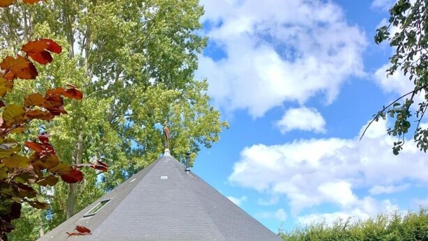 A wooden cabin with a sloped roof, a deck with outdoor furniture, and a patio area. - Le Clos du Héron Perché (HOUDETOT)
