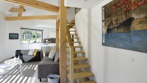 A modern interior with a wooden staircase, a living area with a sofa and coffee table, and a large painting on the wall. - Le Clos du Héron Perché (HOUDETOT)
