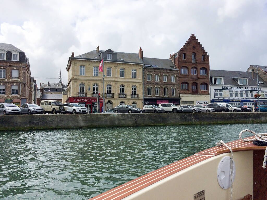 A waterfront view with buildings, a pharmacy, and parked cars.
