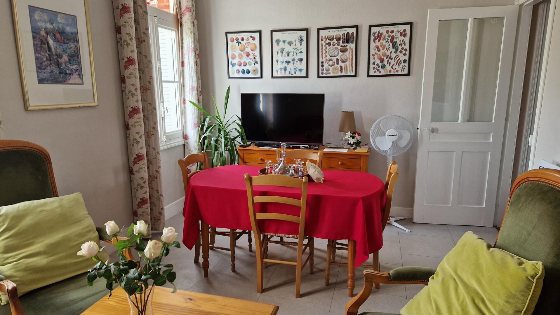 A dining area with a red tablecloth, wooden chairs, a TV, and a fan.