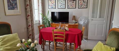 A dining area with a red tablecloth, wooden chairs, a TV, and a fan.