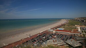 A coastal cityscape with a wide beach, a parking lot, and buildings with a red roof. - Les Amants de Saint Jean (DIEPPE)
