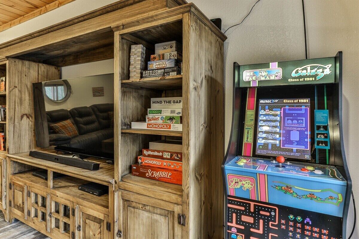 Quarto com unidade de entretenimento de madeira contendo jogos de tabuleiro e uma máquina de arcade retrô.