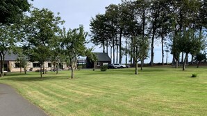 A grassy area with a paved path, trees, and buildings in the background. - Jade - Angerville LA Martel (ANGERVILLE LA MARTEL)