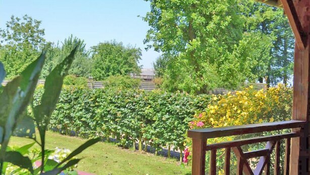 A wooden deck with a view of a well-maintained garden and trees. - Jade - Angerville LA Martel (ANGERVILLE LA MARTEL)