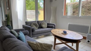 A modern living room with grey sofas, a wooden coffee table, and a view of a garden through large windows. - Jade - Angerville LA Martel (ANGERVILLE LA MARTEL)
