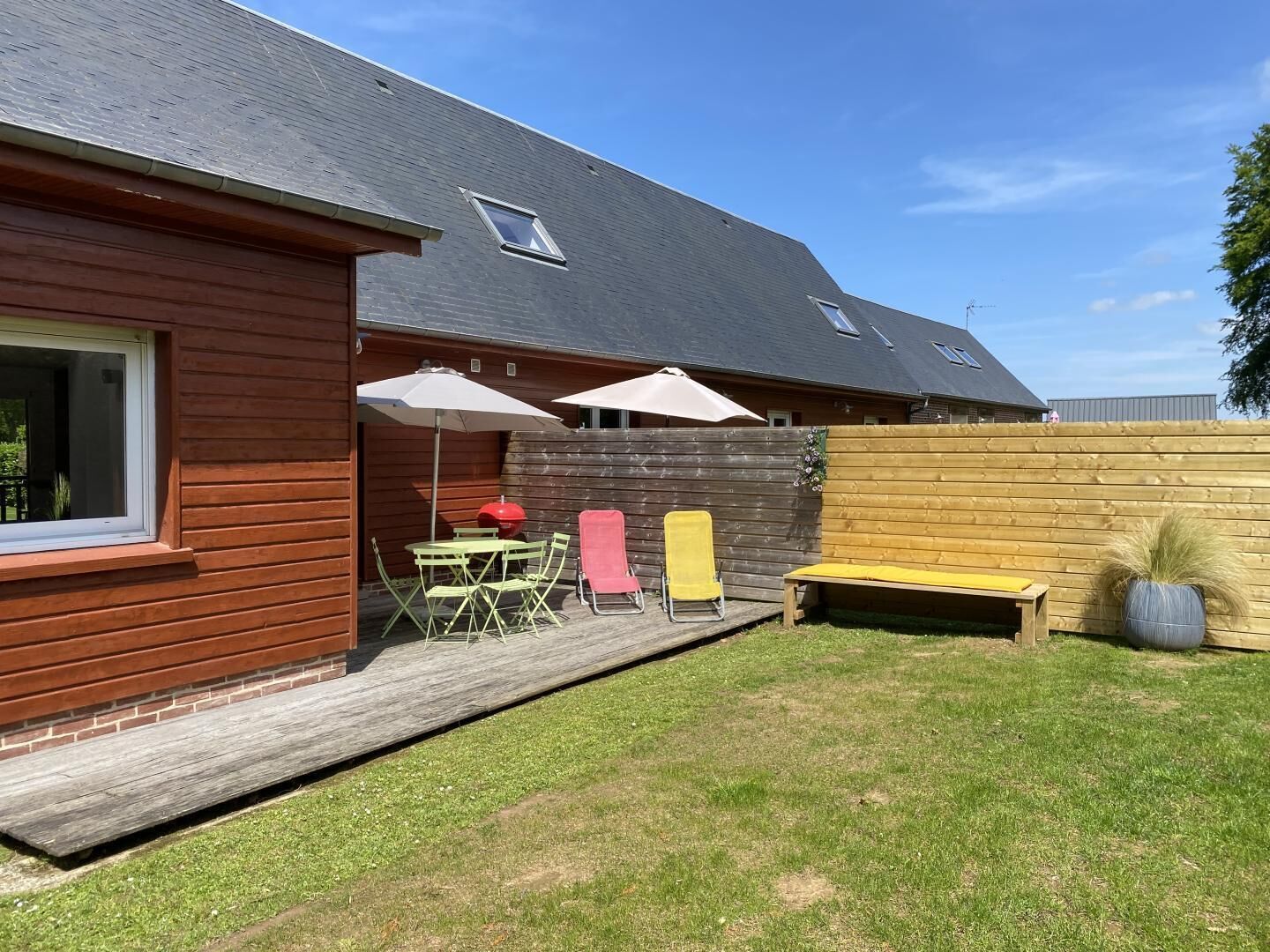 Et hus med træfacade, en overdækket terrasse med bord og stole, samt en indhegnet gård.