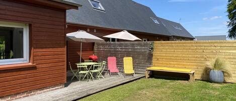Et hus med træfacade, en overdækket terrasse med bord og stole, samt en indhegnet gård.