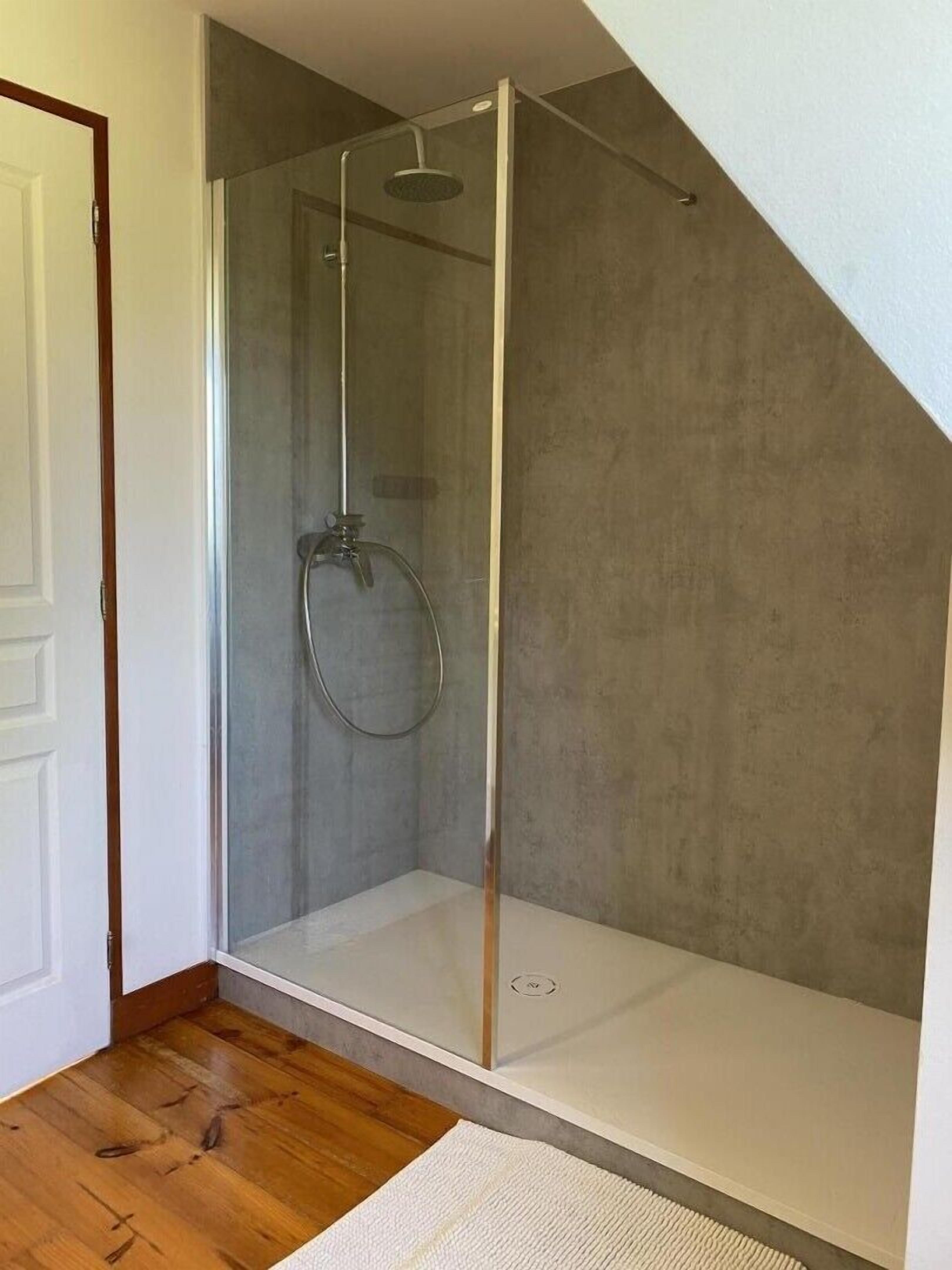 Un box de ducha moderno con puerta de vidrio, un cabezal de ducha y una alcachofa de mano.