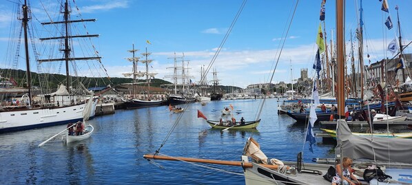 A marina with multiple sailing boats docked, a small rowboat in the foreground, and a building with a tower in the background. - La Corderie - Fecamp (FECAMP)