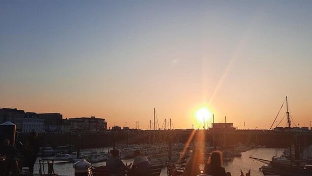 Un puerto deportivo con barcos amarrados, un atardecer de fondo y edificios a lo largo de la costa.