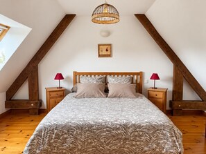 A bedroom with a sloped ceiling, a bed with patterned bedding, two bedside tables with lamps, and a picture on the wall.