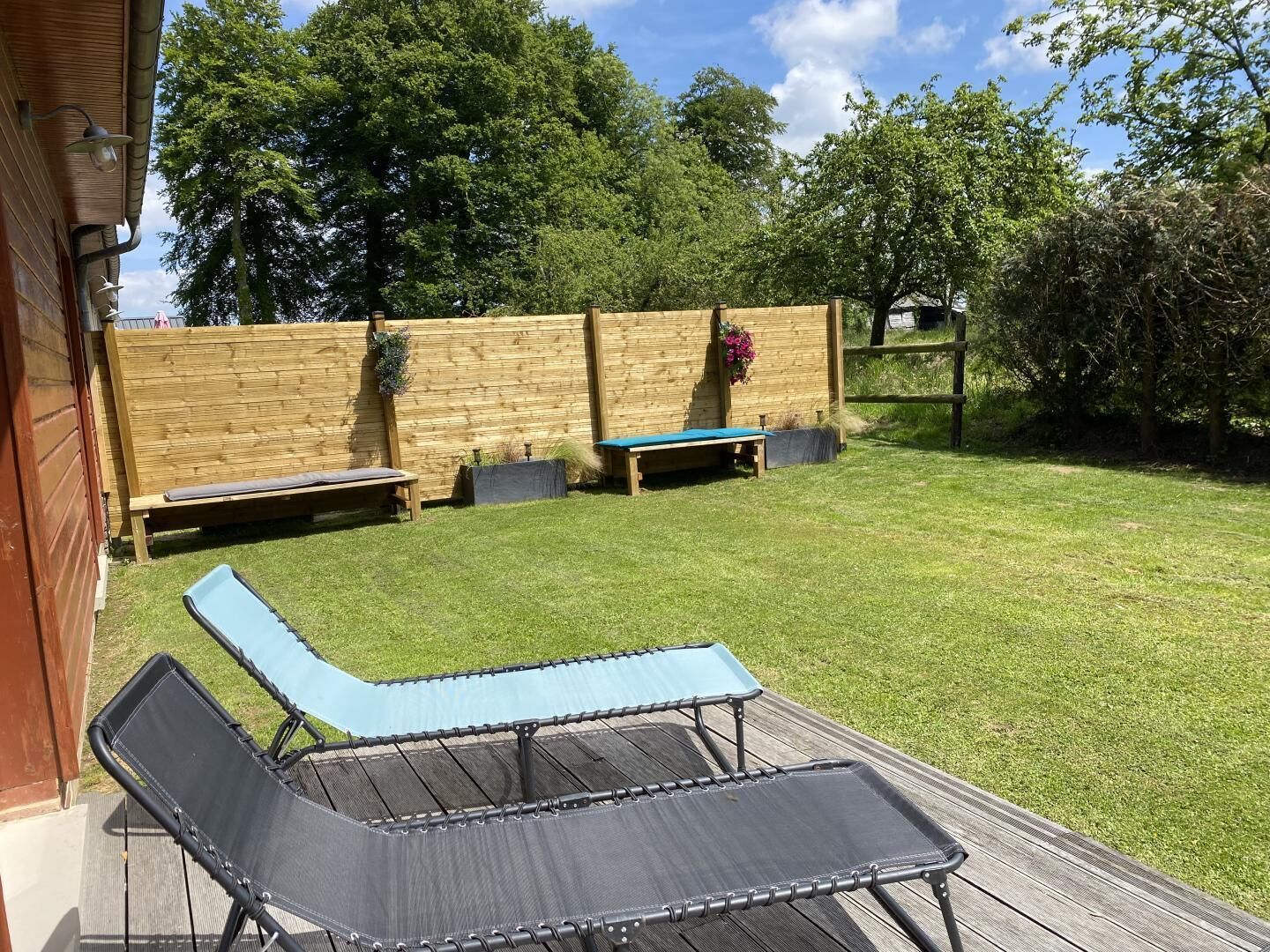 Ein Garten mit einer Holzterrasse, einem blauen Liegestuhl und einem Holzzaun.