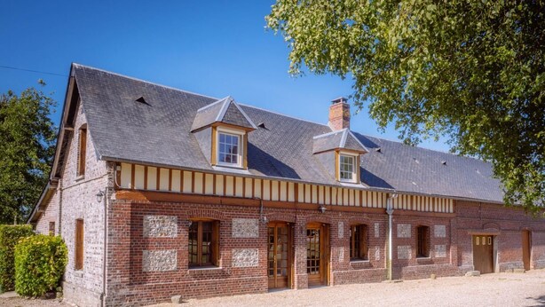 Un bâtiment traditionnel en briques, avec une allée gravillonnée et un grand arbre en arrière-plan.