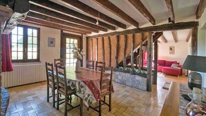 Un coin repas rustique avec une table et des chaises en bois, un mur en pierre et un canapé rouge en arrière-plan.