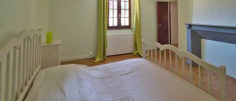 Une chambre avec un lit simple, un radiateur, une fenêtre avec des rideaux et une porte.