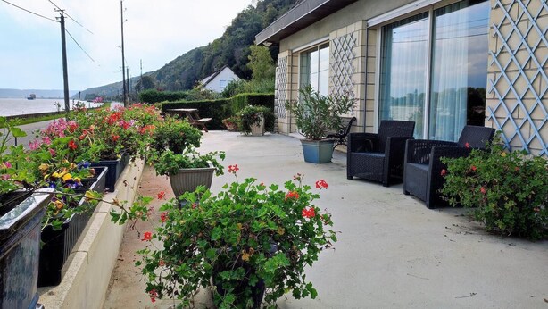 A coastal hotel with outdoor seating, potted plants, and a view of the sea.