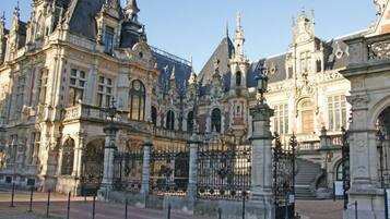 A historic building with ornate architecture, featuring multiple spires and a grand entrance with a gated driveway.