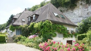 A house with a sloped roof, a small porch, and a garden with pink flowers.