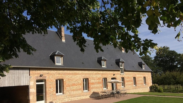 A large brick building with a sloped roof, multiple windows, and a covered outdoor seating area.