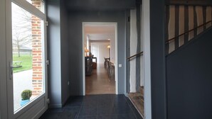 A modern hallway with a dark floor, a staircase on the right, and a view of a dining area in the background.