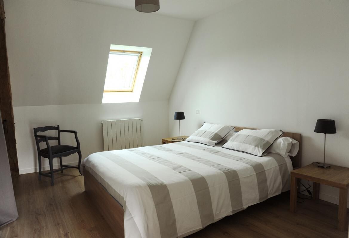 A bedroom with a bed, a chair, a nightstand, a lamp, and a window.