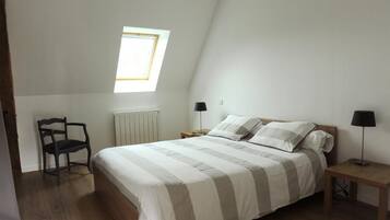 A bedroom with a bed, a chair, a nightstand, a lamp, and a window.
