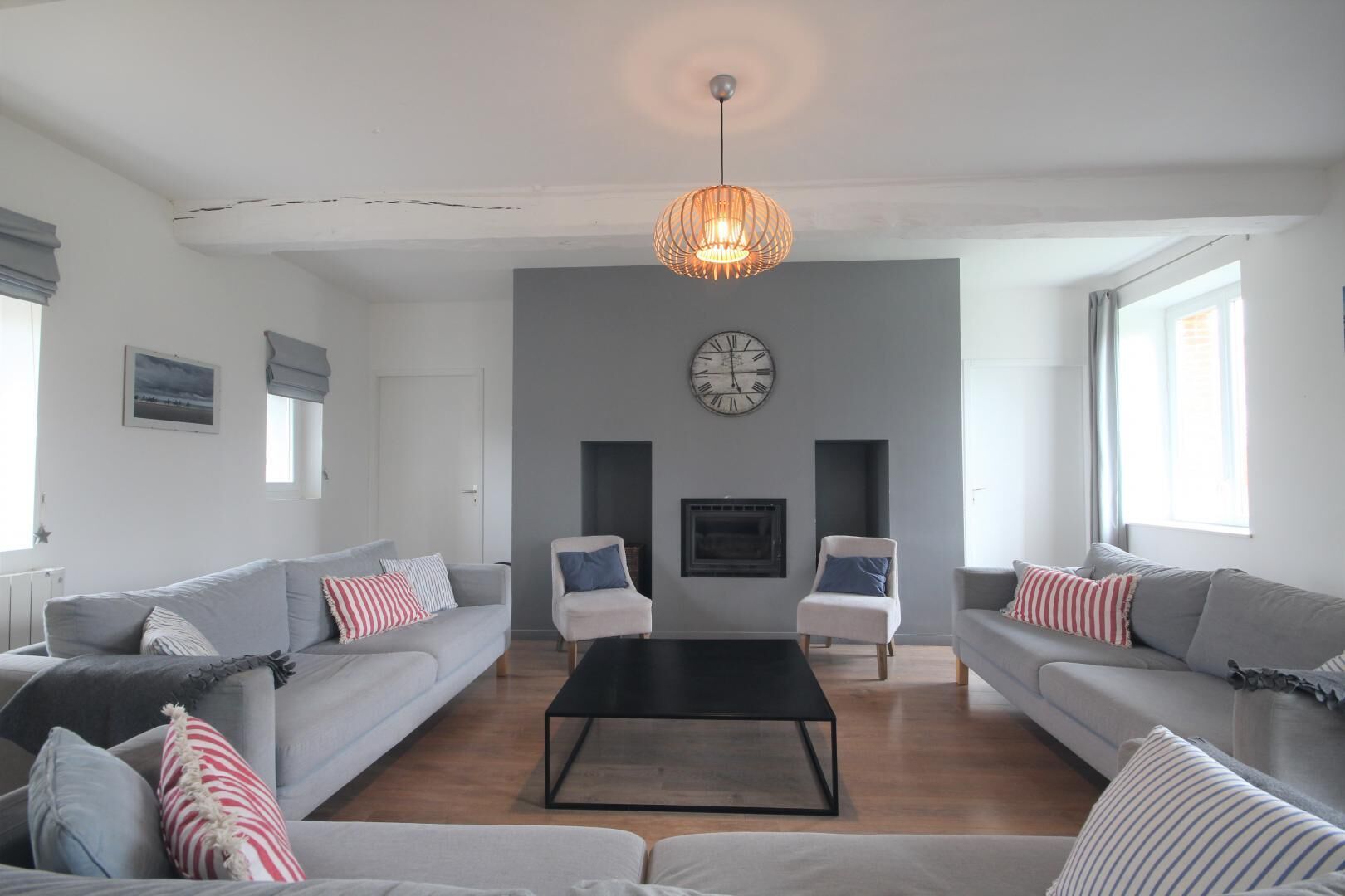 A modern living room with grey sofas, a black coffee table, and a large wall clock.