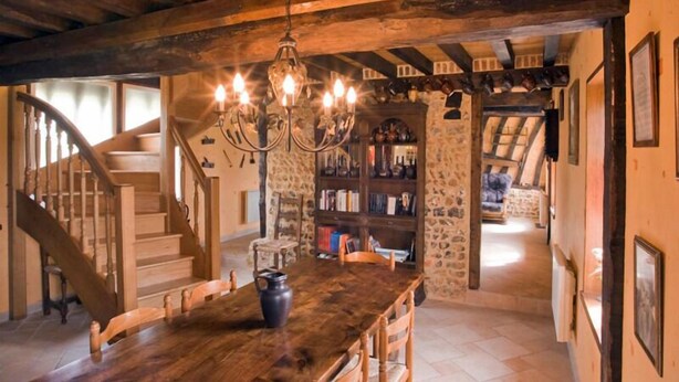 Un intérieur rustique avec un escalier en bois, un lustre, un mur en pierre et une bibliothèque.