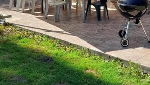 Un patio con una mesa, sillas, una parrilla y un muro de ladrillo.